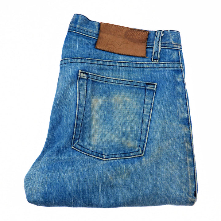 Folded blue denim jeans with a brown leather patch on a white background
