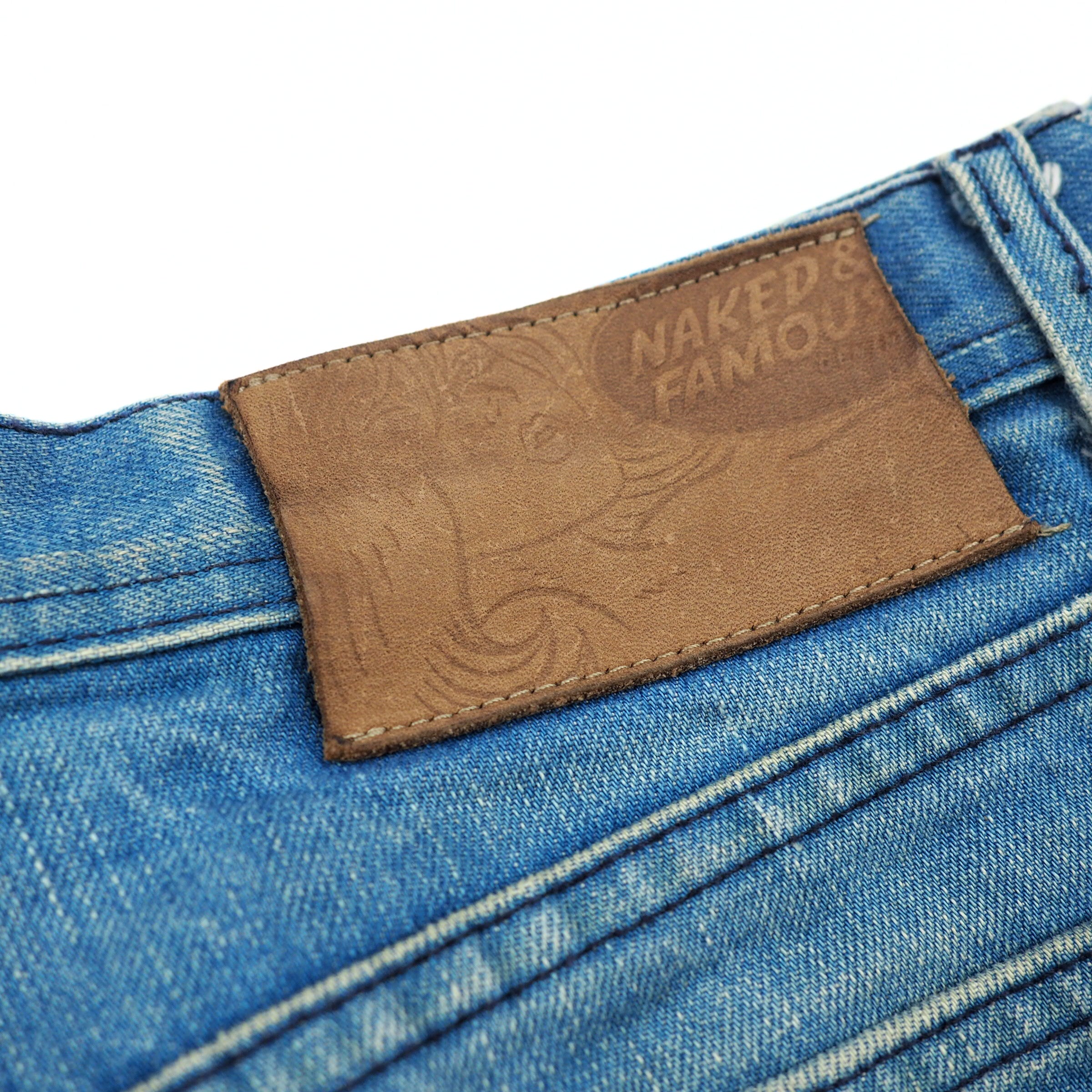 Close-up of a blue denim fabric with a brown leather label featuring 'Naked & Famous' branding.