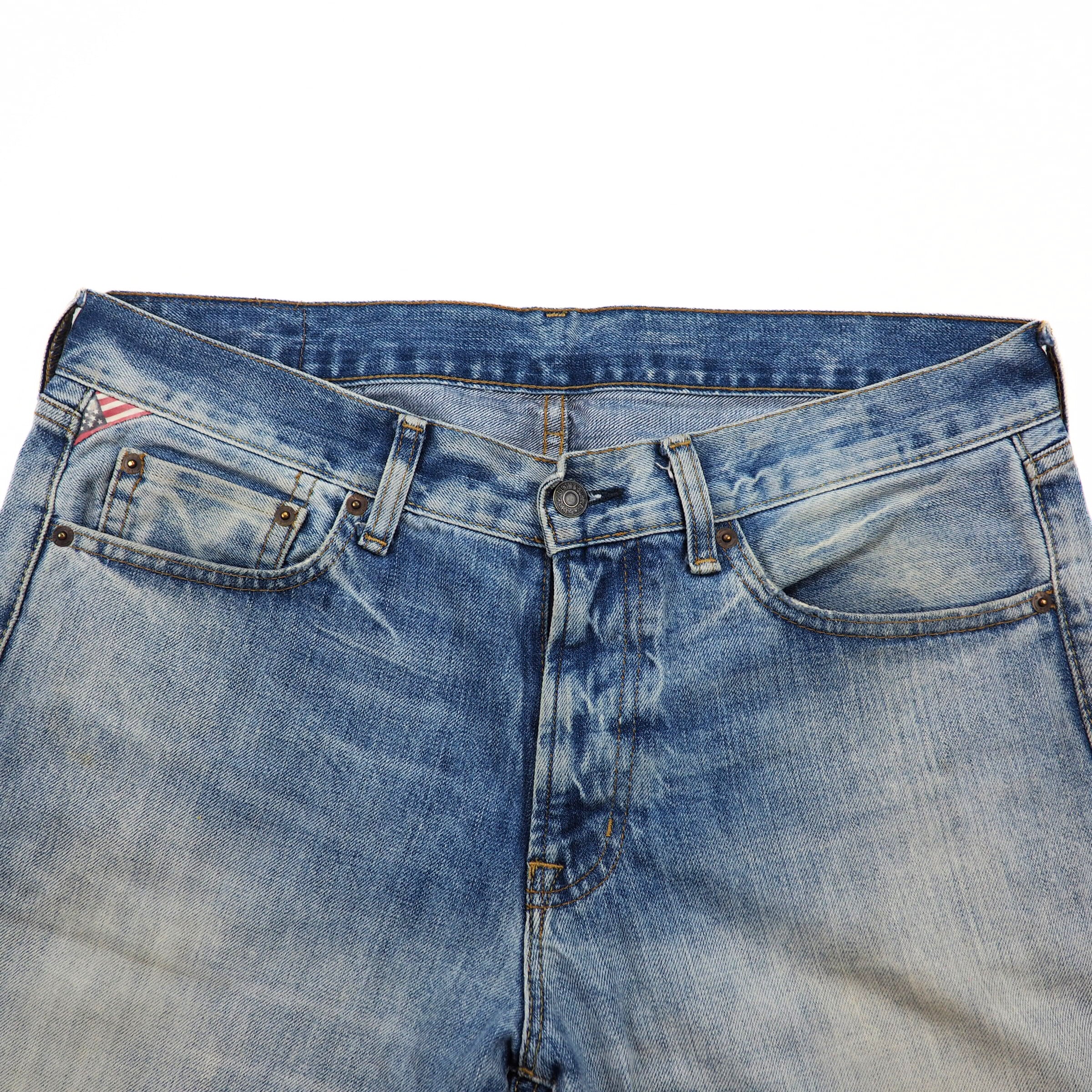 Close up of the waist of a pair of blue denim jeans on a white background