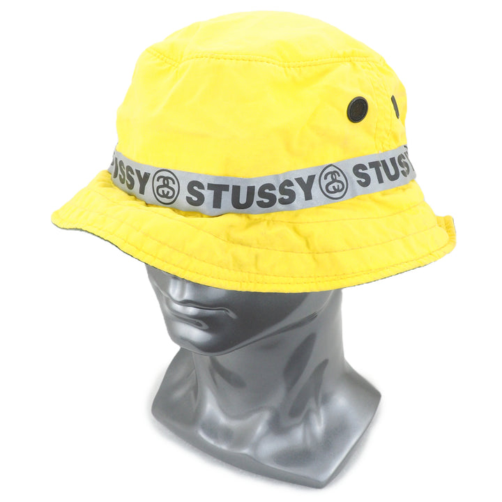Yellow bucket hat with Stussy logo band on a mannequin head against a white background