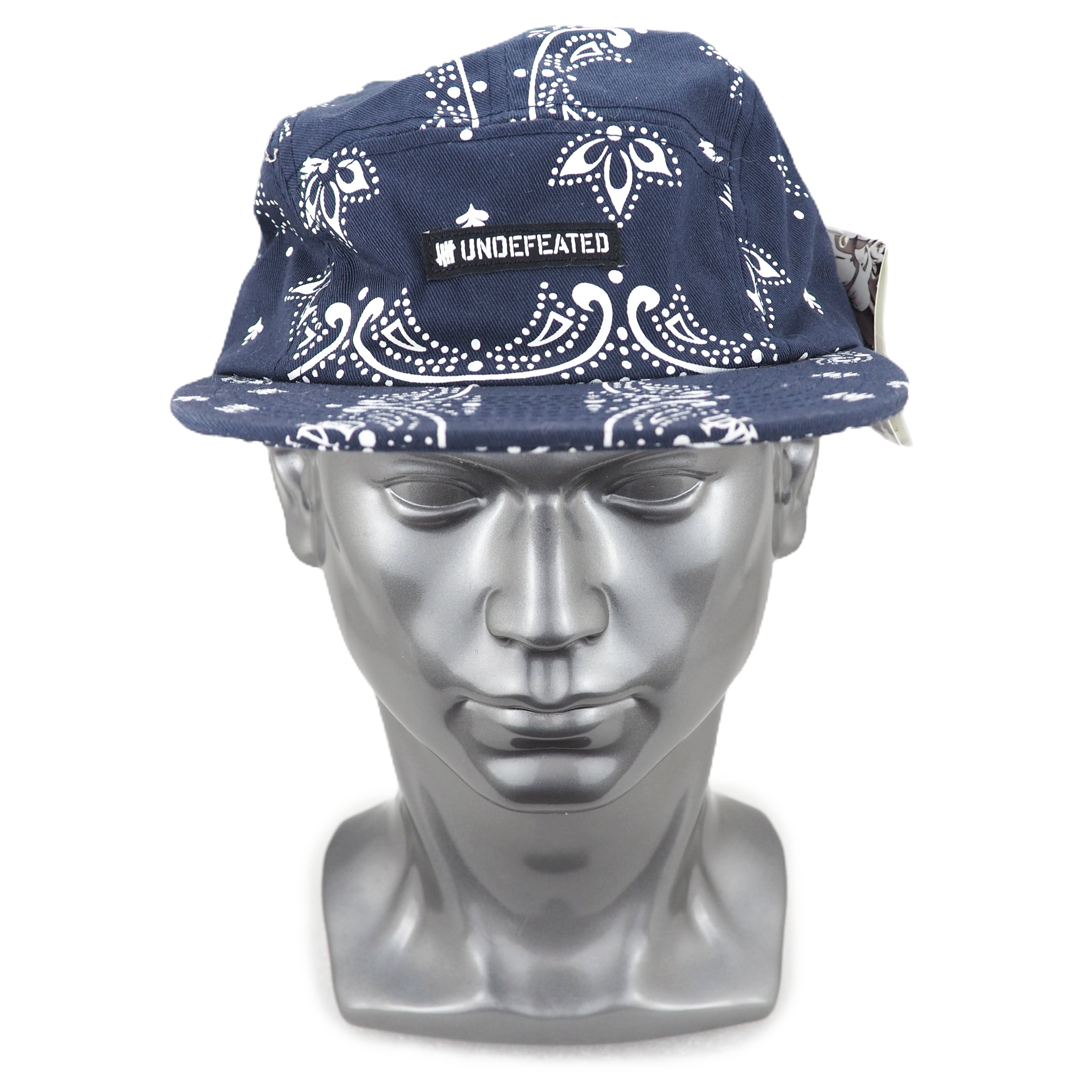Navy blue cap with white paisley patterns on a silver mannequin head against a white background