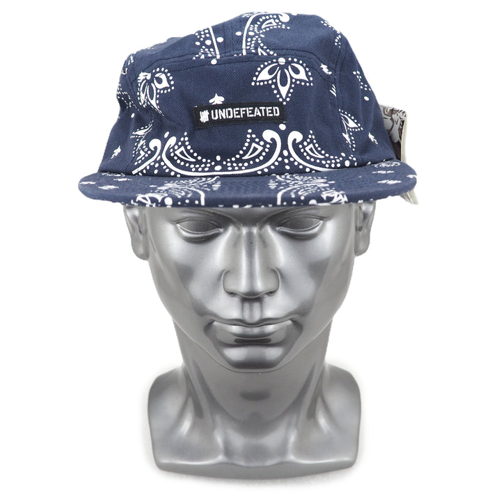 Navy blue cap with white paisley patterns on a silver mannequin head against a white background