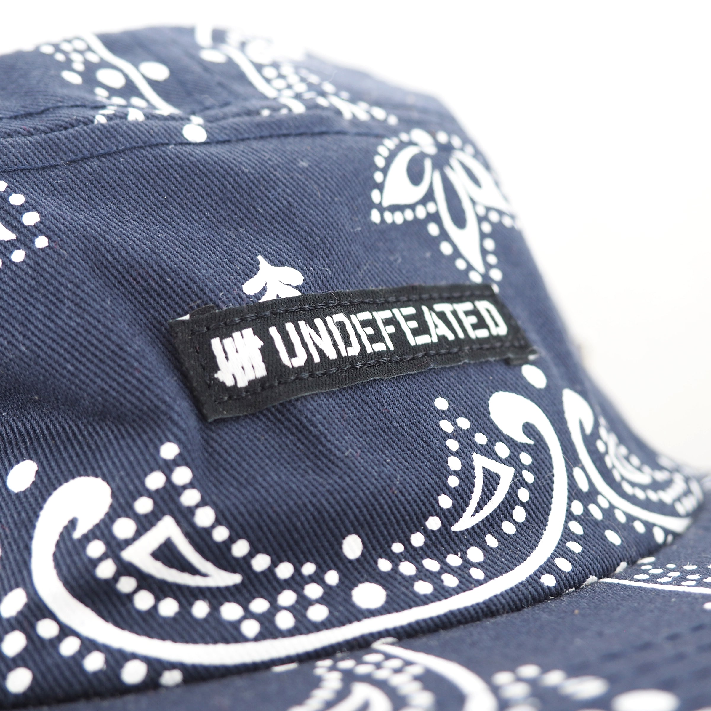 Navy blue cap with white paisley pattern and 'UNDEFEATED' logo.