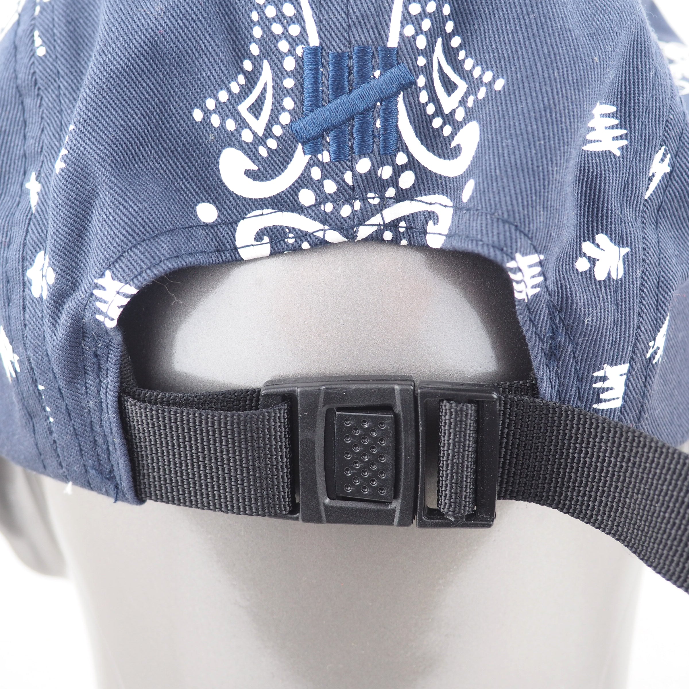 Blue cap with white patterns and black strap on a mannequin head