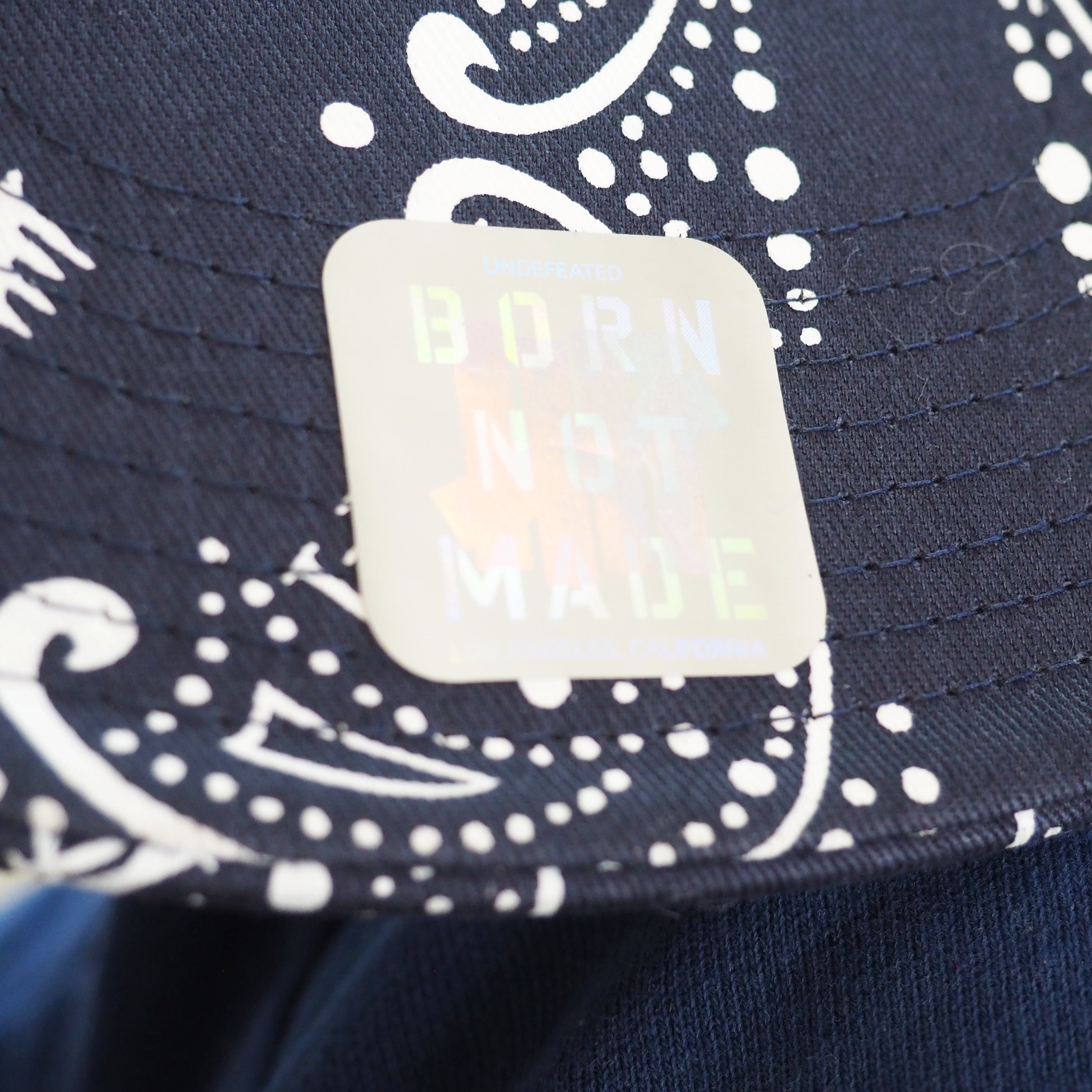 Navy blue cap with white paisly patterns and a reflective label reading 'Born Not Made'