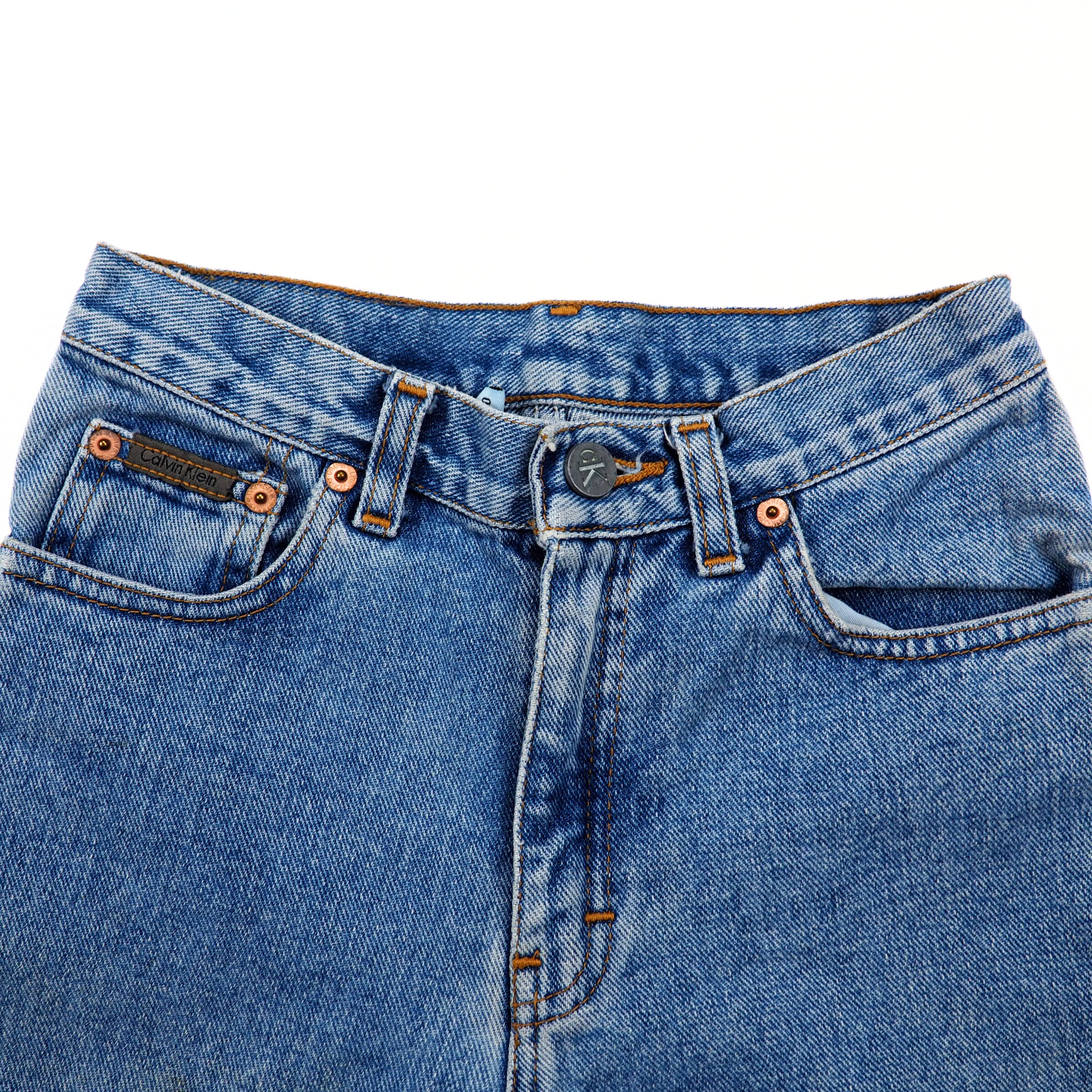 Close-up of the waist area of a pair of blue denim jeans on a white background