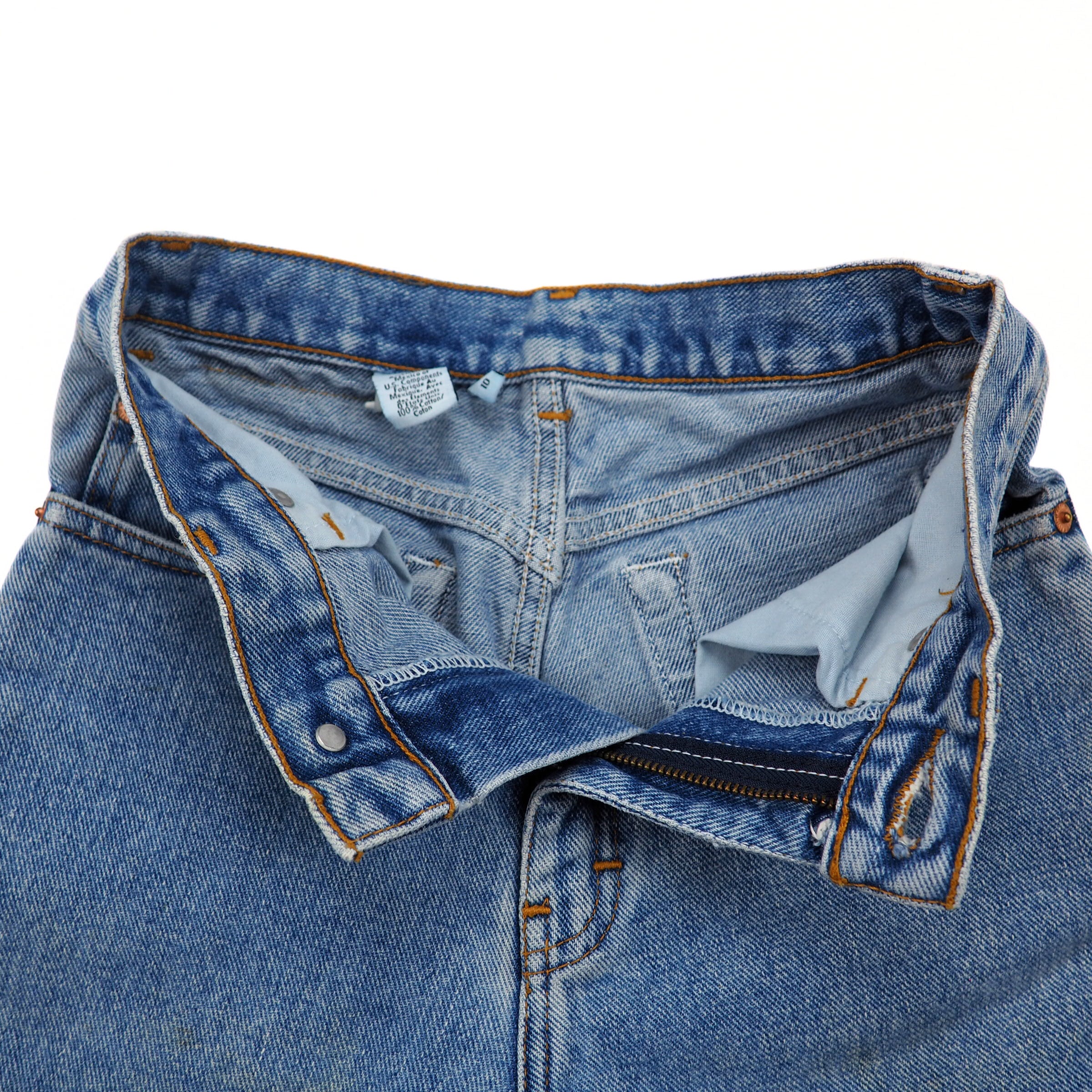 Unzipped pair of blue jeans with a visible inner care label on a white background