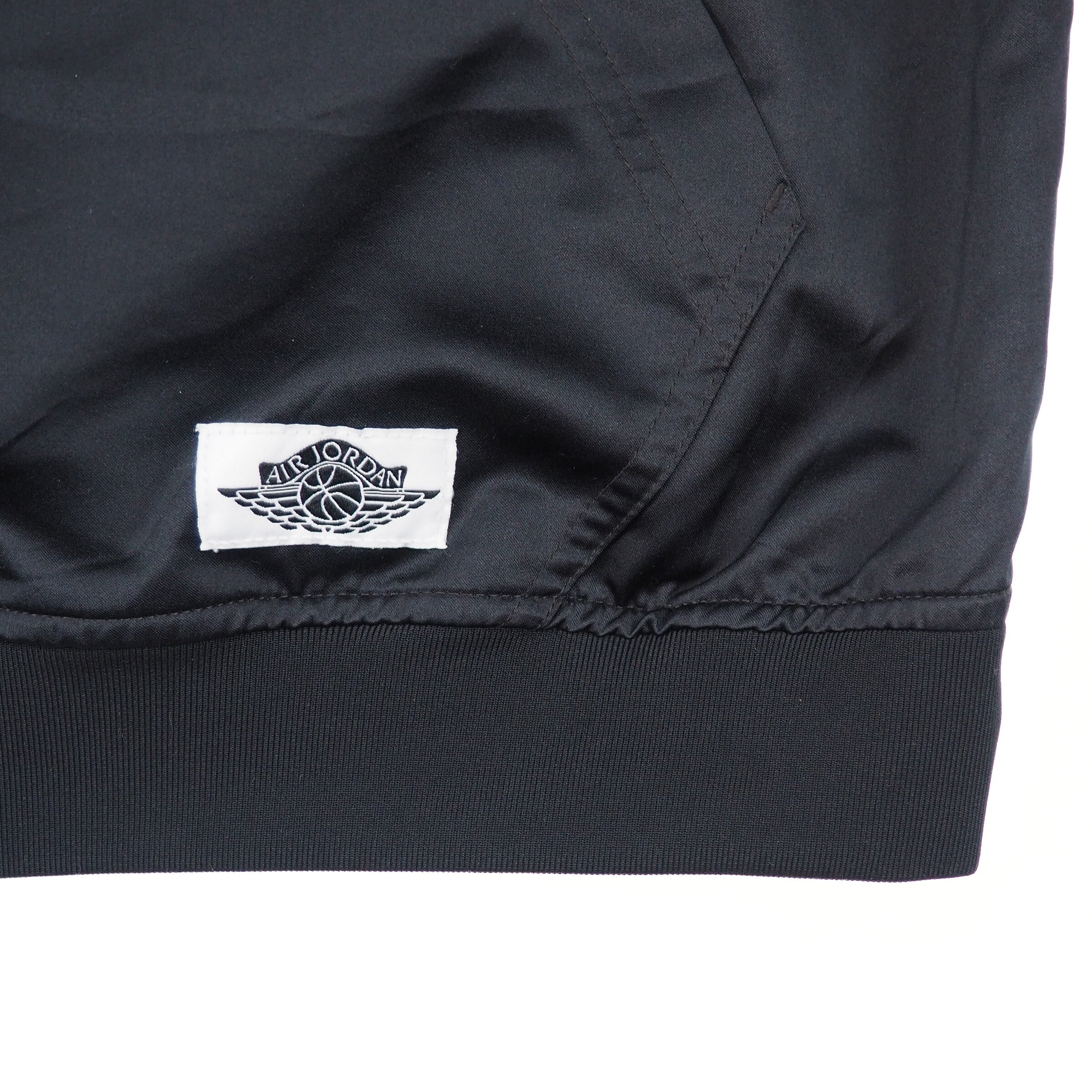 Close-up of a black jacket with a white Air Jordan logo tag on a white background