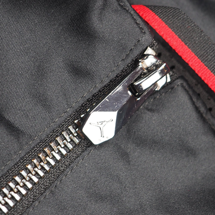 Close-up of a zipper with a Jordan Jumpman logo on a black jacket with red interior lining.