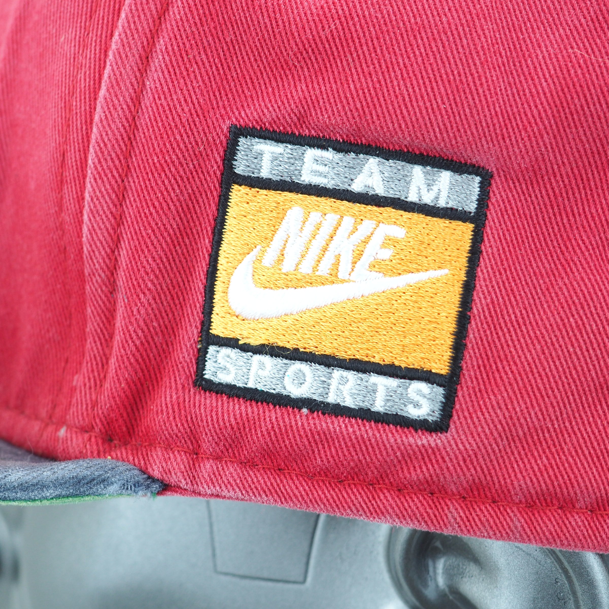 Red cap with a 'Team Nike Sports' patch on a gray background