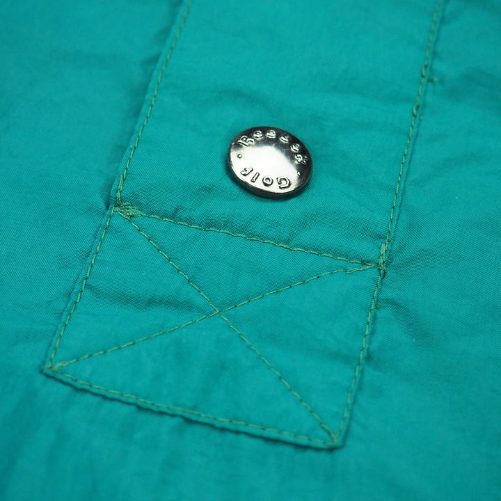 Close-up of a teal fabric pocket with a button featuring 'Reebok Golf' branding.